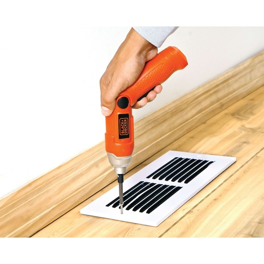 BLACKDECKER 9036 cordless screwdriver used to fasten a vent cover on a wood floor, close-up angle.