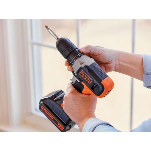 BLACKDECKER BCD702C1 cordless drill with orange and black design, held in hands near a window.