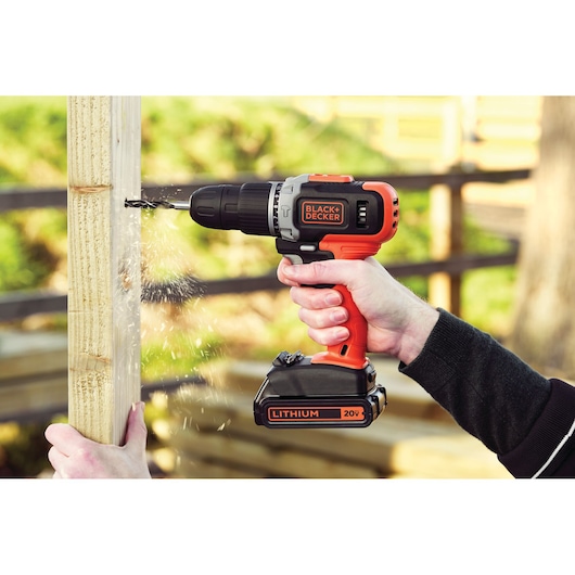 BLACK+DECKER BCK21S1S cordless drill 20V in use, drilling into wood, outdoor setting.