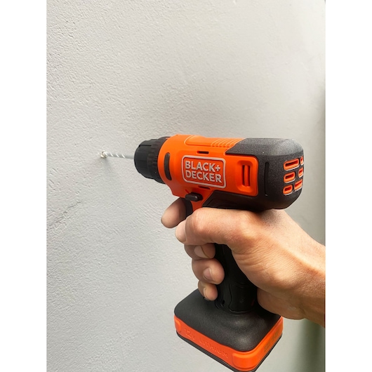 BLACK+DECKER BCD712VHD orange and black cordless drill in hand drilling into a wall, side view.