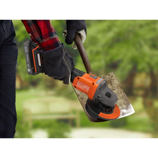 BLACKDECKER BCG6L8B cordless angle grinder being used to sharpen a garden tool, outdoor setting.