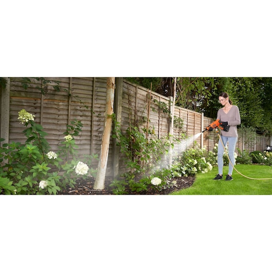 Photo of person using BLACKDECKER BCPC20D1 cordless pressure washer with hose to water garden plants outdoors.