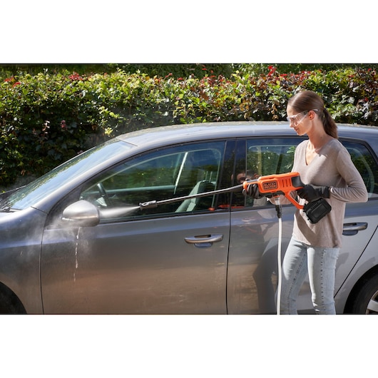 Person using BLACKDECKER BCPC20D1 cordless pressure washer to clean a gray car outdoors.