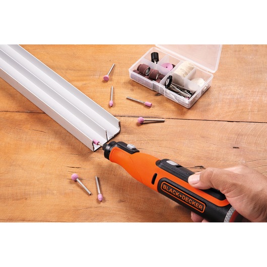 BLACK+DECKER rotary tool BCRT8K35 used for grinding metal, with accessory kit and attachments on wood surface.