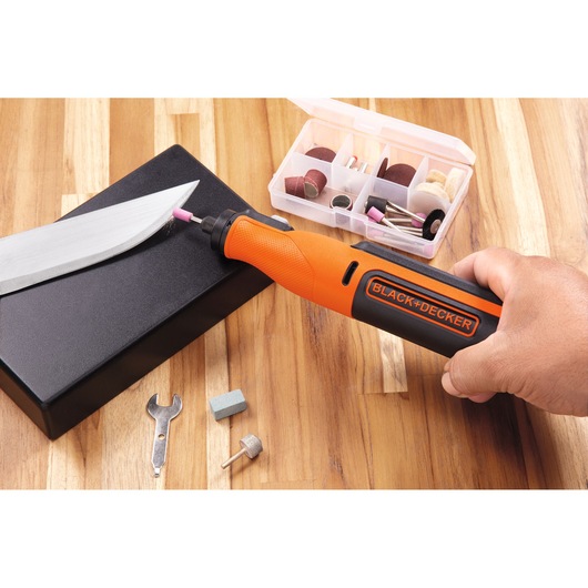 Photo of BLACK+DECKER BCRT8K35 rotary tool in use sharpening a knife, accessories case visible on wooden surface.