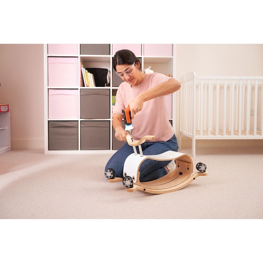 BLACKDECKER BCRTA601I cordless screwdriver being used to assemble a child's wooden ride-on toy in a nursery.