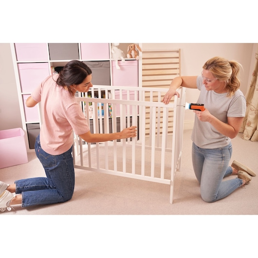 BLACKDECKER BCRTA601I cordless screwdriver in use while assembling white baby crib in a nursery room.