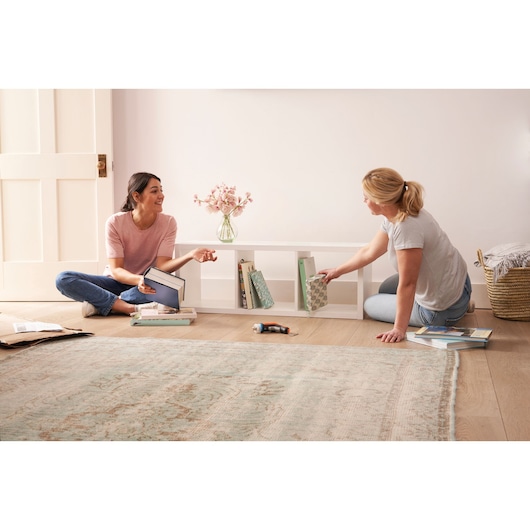 BLACKDECKER BCRTA601I cordless screwdriver on floor with two women organizing books in living room.