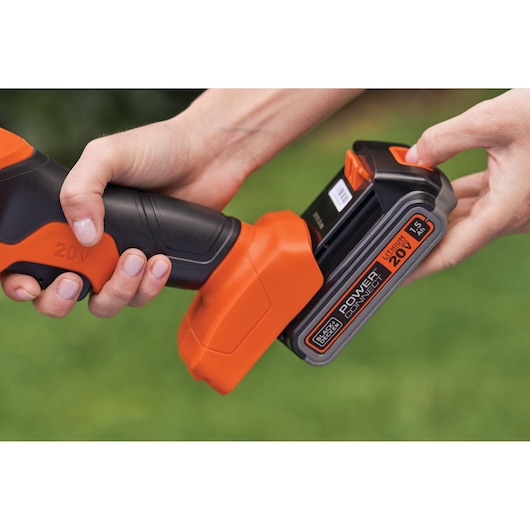 Close-up photo of BLACK+DECKER BCSS820C1 hedge trimmer, hands attaching 20V lithium battery outdoors.