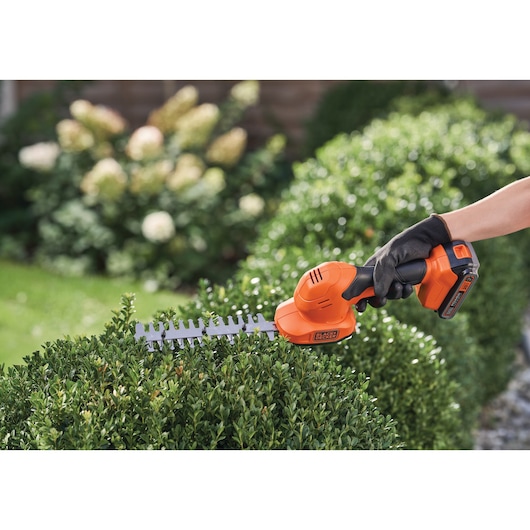 BLACK+DECKER BCSS820C1 cordless shrub shear in use trimming green hedge outdoors.