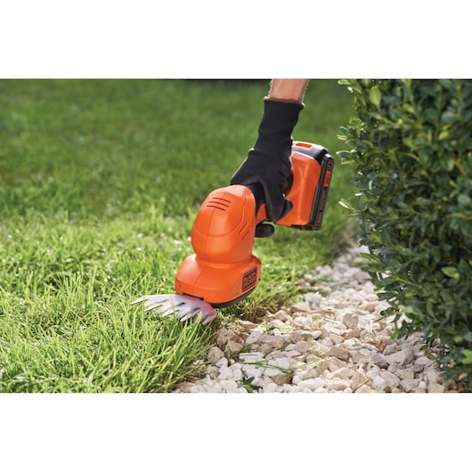 BLACK+DECKER BCSS820C1 cordless grass shear trimming lawn edge next to rocks and bushes.