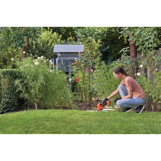 Person using BLACKDECKER BCSS820C1 cordless grass shear and shrub trimmer in garden next to flower bed.