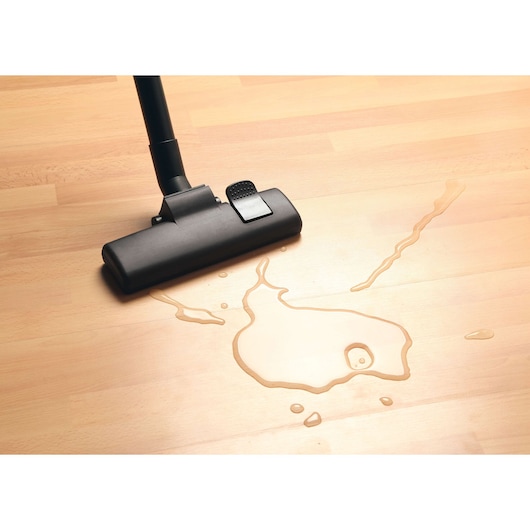 BLACKDECKER BDWD10 vacuum cleaner nozzle cleaning liquid spill on light wood floor, top view.