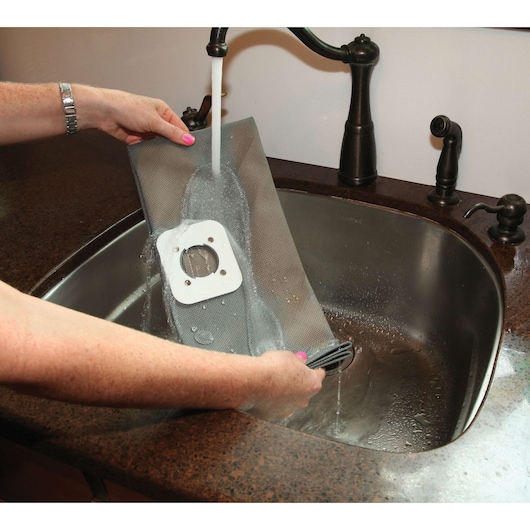 BLACKDECKER BDWD15 vacuum filter being rinsed under faucet in kitchen sink, person holding filter.