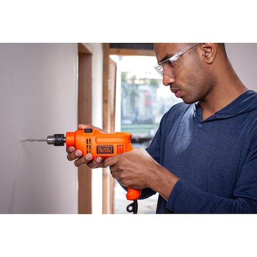 Person using BLACK+DECKER corded drill BED710450 to drill into a wall, handheld operation, orange and black tool.