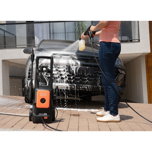 Photo of BLACKDECKER BEPW1520L pressure washer used to clean a black car in a driveway, soap and spray visible.