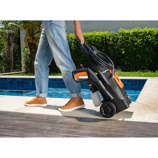 BLACKDECKER BEPW1520L pressure washer being wheeled by a person in casual jeans and brown shoes beside a pool.