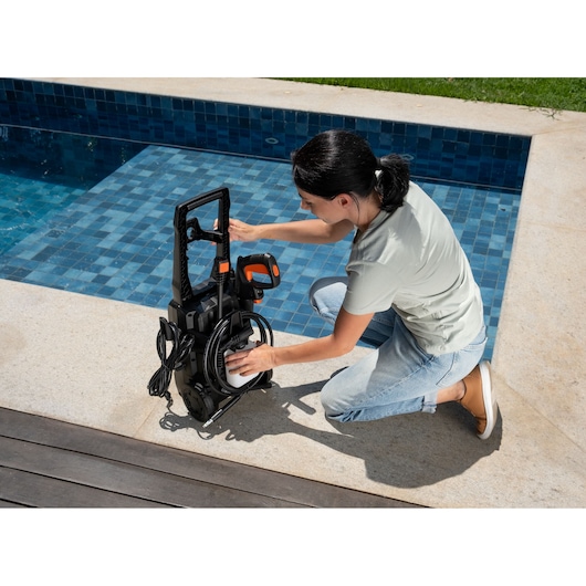 BLACKDECKER BEPW1520L pressure washer by a poolside, person adjusting hose attachment.