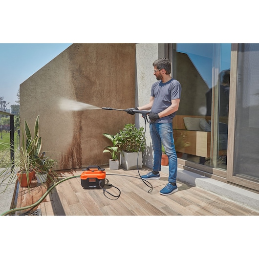BLACKDECKER BEPW1600H pressure washer cleaning outdoor wall, man holding spray wand, orange and black unit on patio.