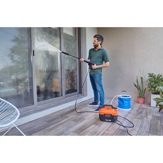 BLACKDECKER BEPW1600H pressure washer in use cleaning glass doors on a patio with a portable blue water bucket.