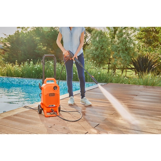 BLACKDECKER BEPW1800T pressure washer cleaning wooden deck near pool outdoors.