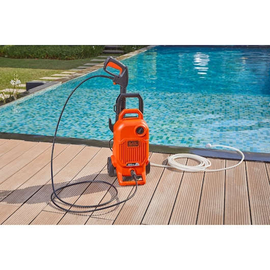 BLACKDECKER BEPW1800T pressure washer with hose placed by a pool on wooden decking.