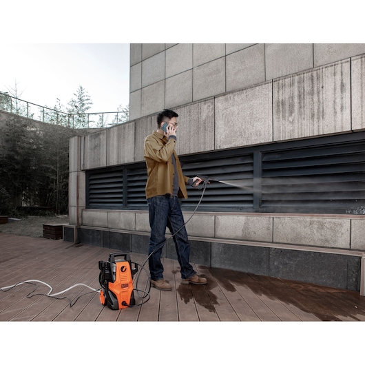 Photo of BLACKDECKER BEPWB1740 pressure washer in use, cleaning a wall outdoors, orange and black design visible.