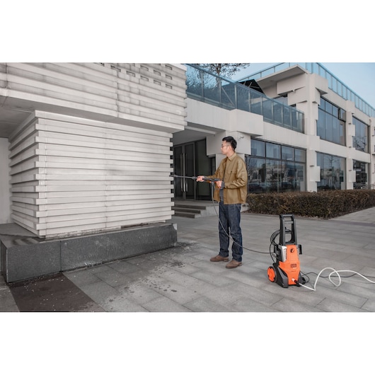 BLACKDECKER BEPWB2000 pressure washer cleaning building exterior, person using orange unit on sidewalk.