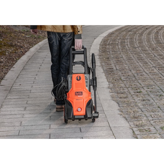 BLACKDECKER BEPWB2000 pressure washer with orange and black design being wheeled on a sidewalk outdoors.