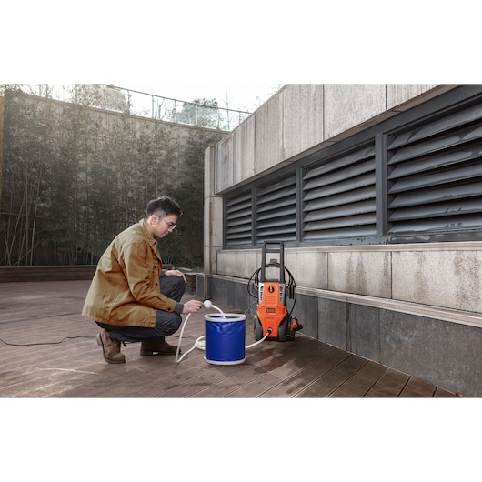 Photo of BLACKDECKER BEPWB2000 pressure washer in use outdoors with a person filling water from a blue bucket.