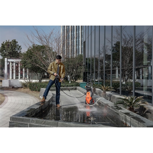 BLACKDECKER BEPWB2400 pressure washer used outdoors on pavement near modern building.