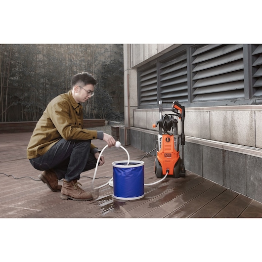 Photo of BLACK+DECKER BEPWB2400 pressure washer on patio, connected to blue water bucket and hose.