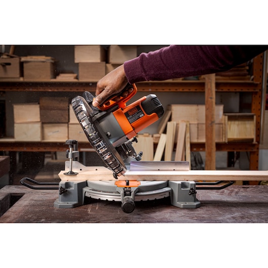 BLACKDECKER BES7101800MS miter saw in use, orange and black, cutting wood in a workshop.