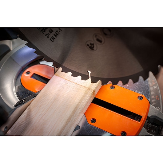 BLACKDECKER BES7101800MS miter saw close-up cutting wood, silver blade and orange base, photography.