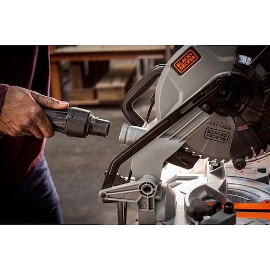 Photo of BLACK+DECKER BES7101800MS miter saw, close-up of dust extraction port being connected in workshop.