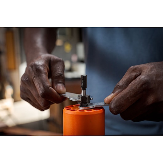BLACKDECKER BETR0500 tool use, hands adjusting metal component on orange cylinder in workshop.