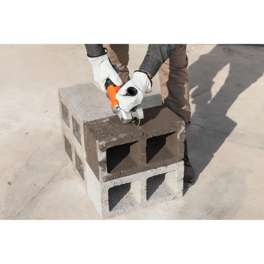 Photo of BLACKDECKER G720X angle grinder in use cutting a concrete block, gloves visible, outdoor setting.