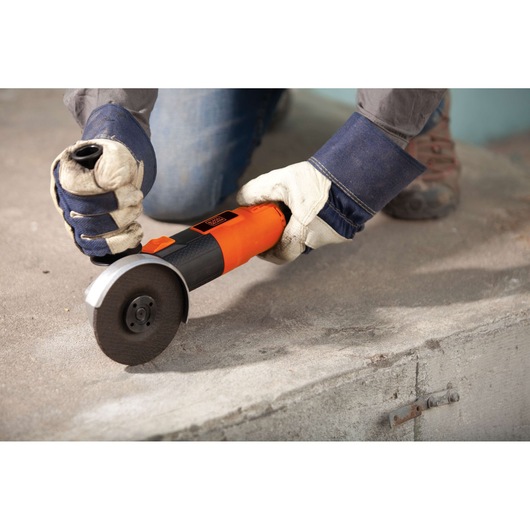 BLACKDECKER G720 angle grinder in use on concrete, worker wearing gloves and denim sleeves.