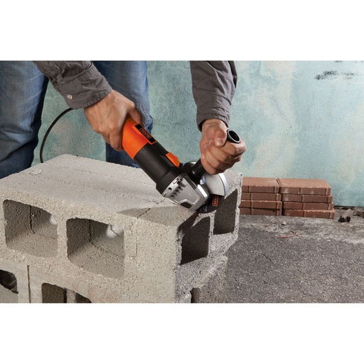 Photo of BLACKDECKER G720 angle grinder used to cut a concrete block, showing tool in operation.