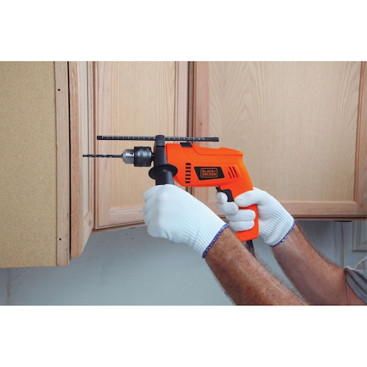 Photo of BLACKDECKER HD555 orange corded drill in use, drilling wood cabinet, gloved hands holding handle.