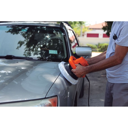 Photo of a person using BLACKDECKER KP12K car polisher on a gray car hood outdoors.