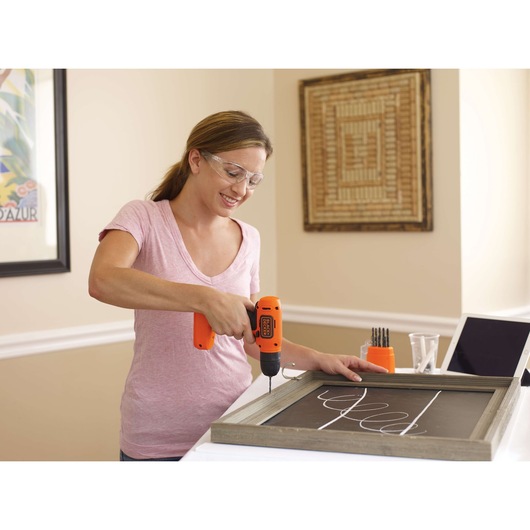 Photo of person using BLACKDECKER LD008 orange cordless drill on a framed chalkboard, bit set visible on table.