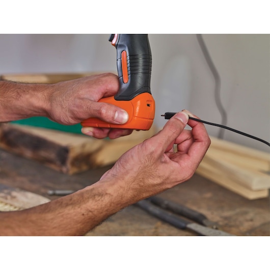 BLACKDECKER LD008 cordless screwdriver being charged with a USB cable in a workshop.
