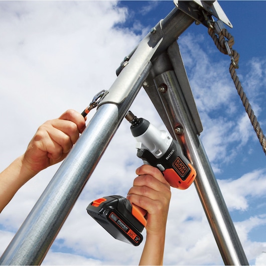 Photo of BLACKDECKER MTX20K6A cordless drill being used on outdoor metal pipes under blue sky.