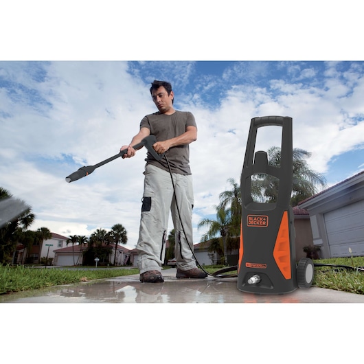 BLACK+DECKER PW1370TDL pressure washer in use outdoors on a driveway, visible orange accents.