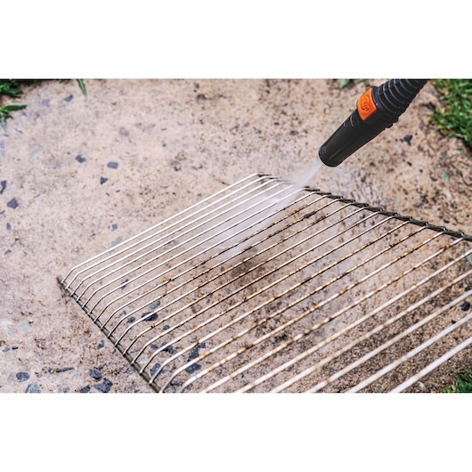 BLACKDECKER PW1450TD pressure washer cleaning a metal grill on a stone surface.