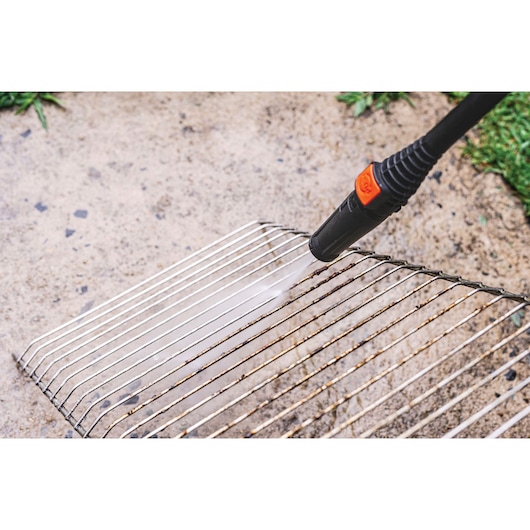 BLACKDECKER PW1450TD pressure washer cleaning a metal grill outdoors, close-up view.