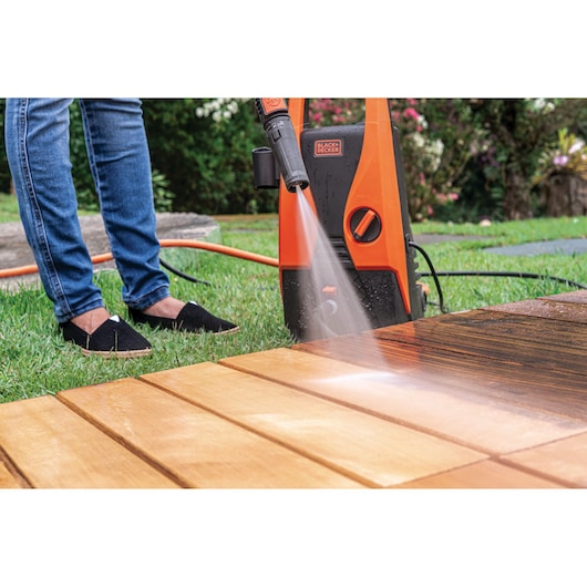BLACKDECKER PW1450TD pressure washer cleaning wooden deck outdoors, orange unit with spray nozzle.