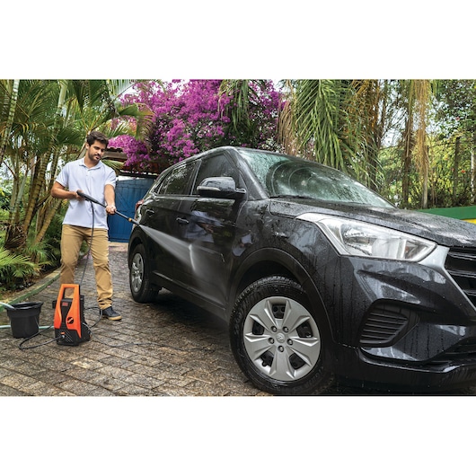 BLACKDECKER PW1450TD pressure washer used outdoors to clean a black SUV, surrounded by plants.