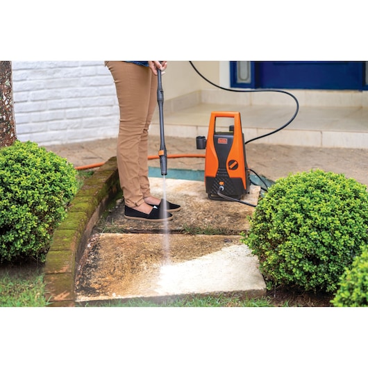 Photo of BLACKDECKER PW1450TD pressure washer cleaning outdoor pavement near shrubs.